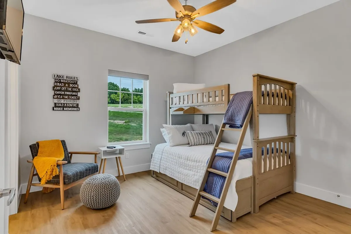 A playful kids’ bunk room with a twin-over-full bunk bed, a comfortable chair, a whimsical decorative sign, and a window view. The playful decor and flexible sleeping arrangements invite imaginative play and bonding moments.