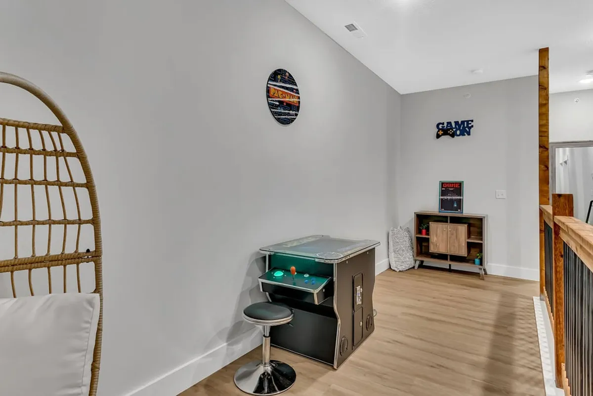 This fun, inviting interior image showcases an arcade game, a hanging chair, and wall decorations, creating a playful and social space. The room invites friendly competition and shared moments, perfect for group retreats and entertaining guests after a day exploring Branson.