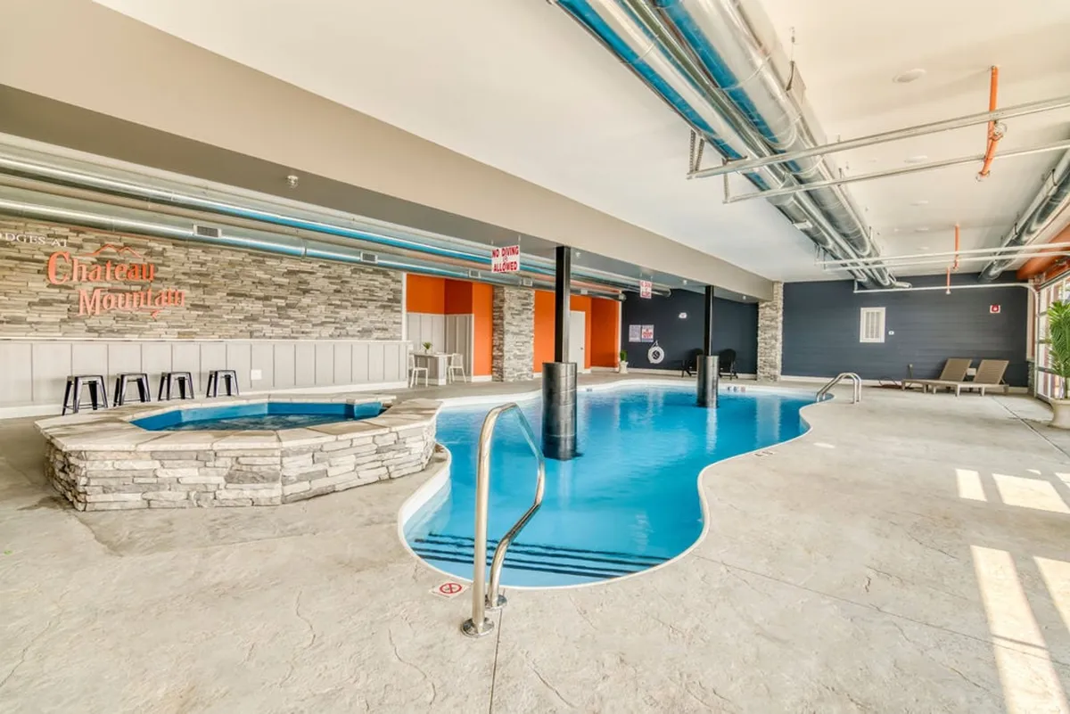 An inviting indoor pool area with a sparkling swimming pool, hot tub, and the Chateau Mountain sign, offering a glimpse of comfortable seating areas ideal for gathering and relaxation. The mood is tranquil yet social, suitable for year-round enjoyment.