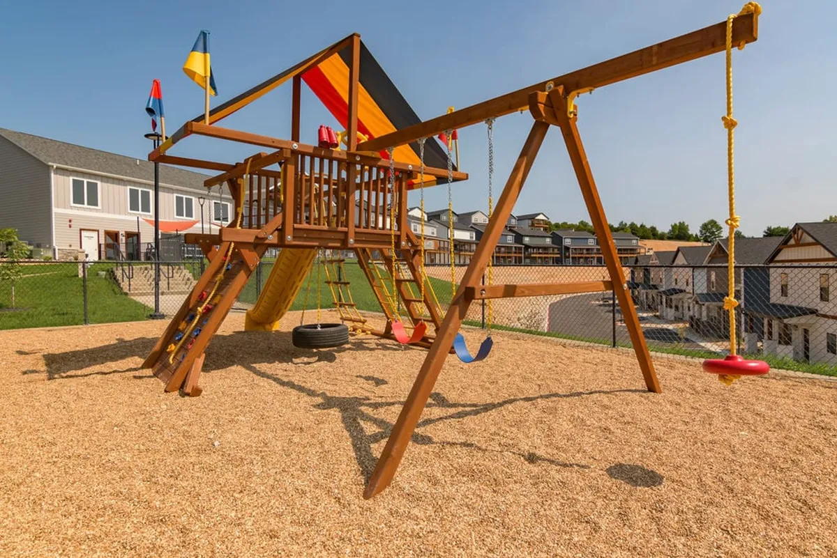 A joyful outdoor playground scene featuring a colorful structure, swings, flags, and a sandbox area. Children can be seen playing, capturing the spirit of family fun and outdoor play just beyond the lodge.