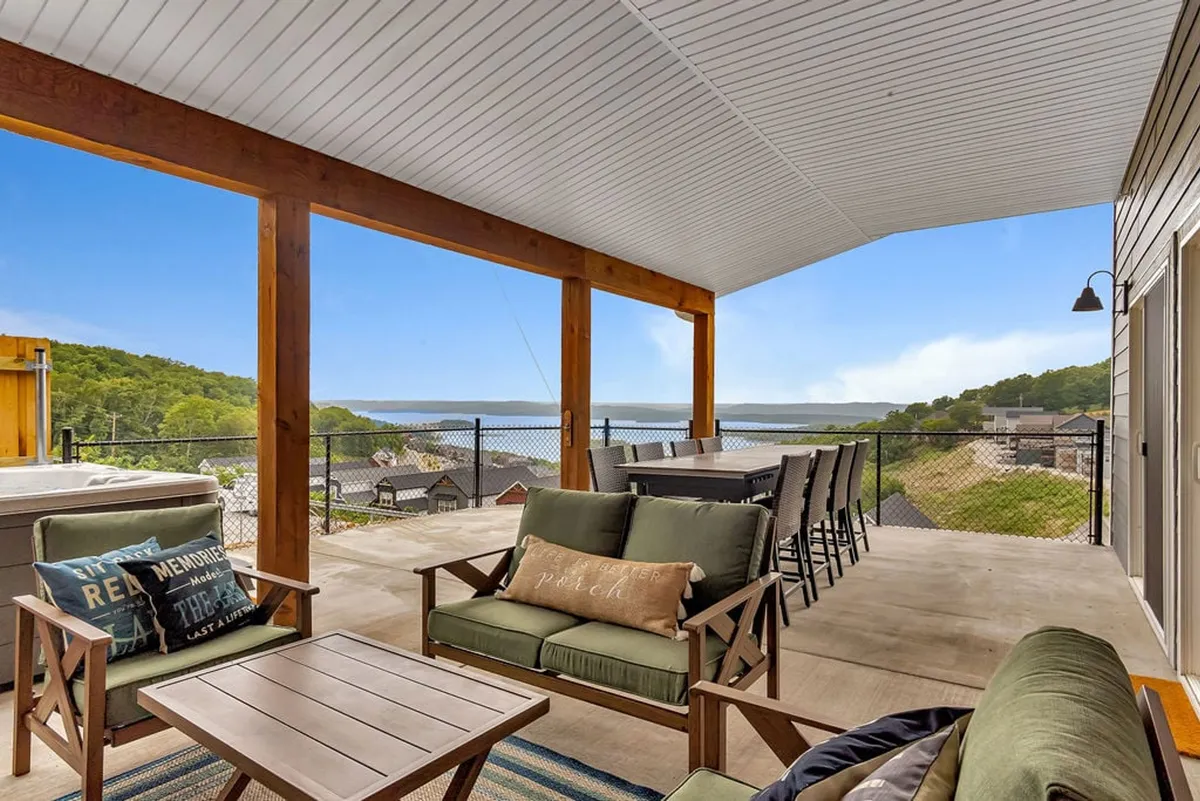 An inviting exterior scene with a spacious patio furnished for relaxation and entertaining. Comfortable seating is arranged to maximize enjoyment of the expansive lake view, framed by warm wooden beams and soft natural light. The tranquil mood suggests moments of coffee at sunrise or sunset gatherings with loved ones.