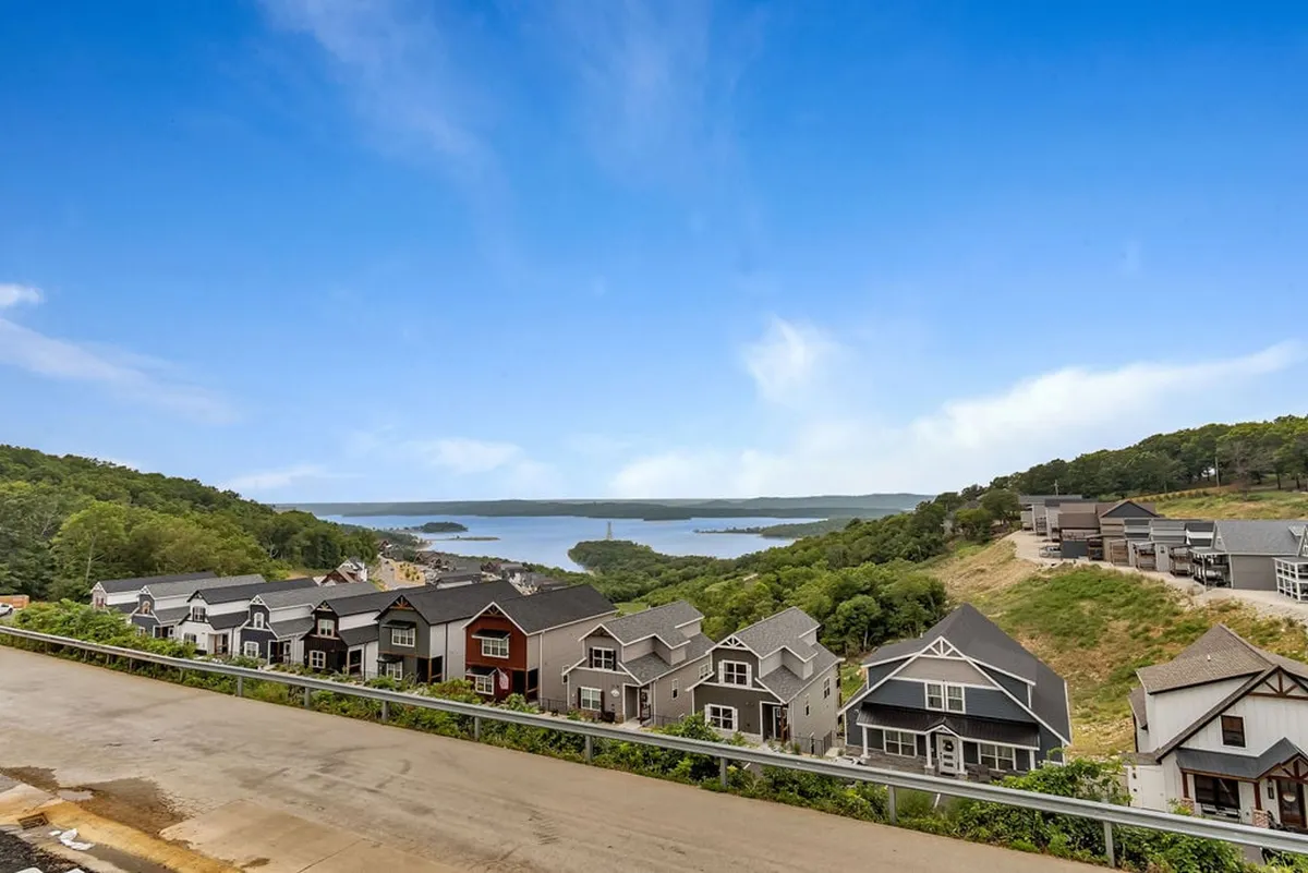 A sweeping view of Table Rock Lake with tree-covered hills in the background and houses dotting the shoreline. The tranquil water reflects the sky, creating a picturesque backdrop ideal for family photos and lakeside gatherings.