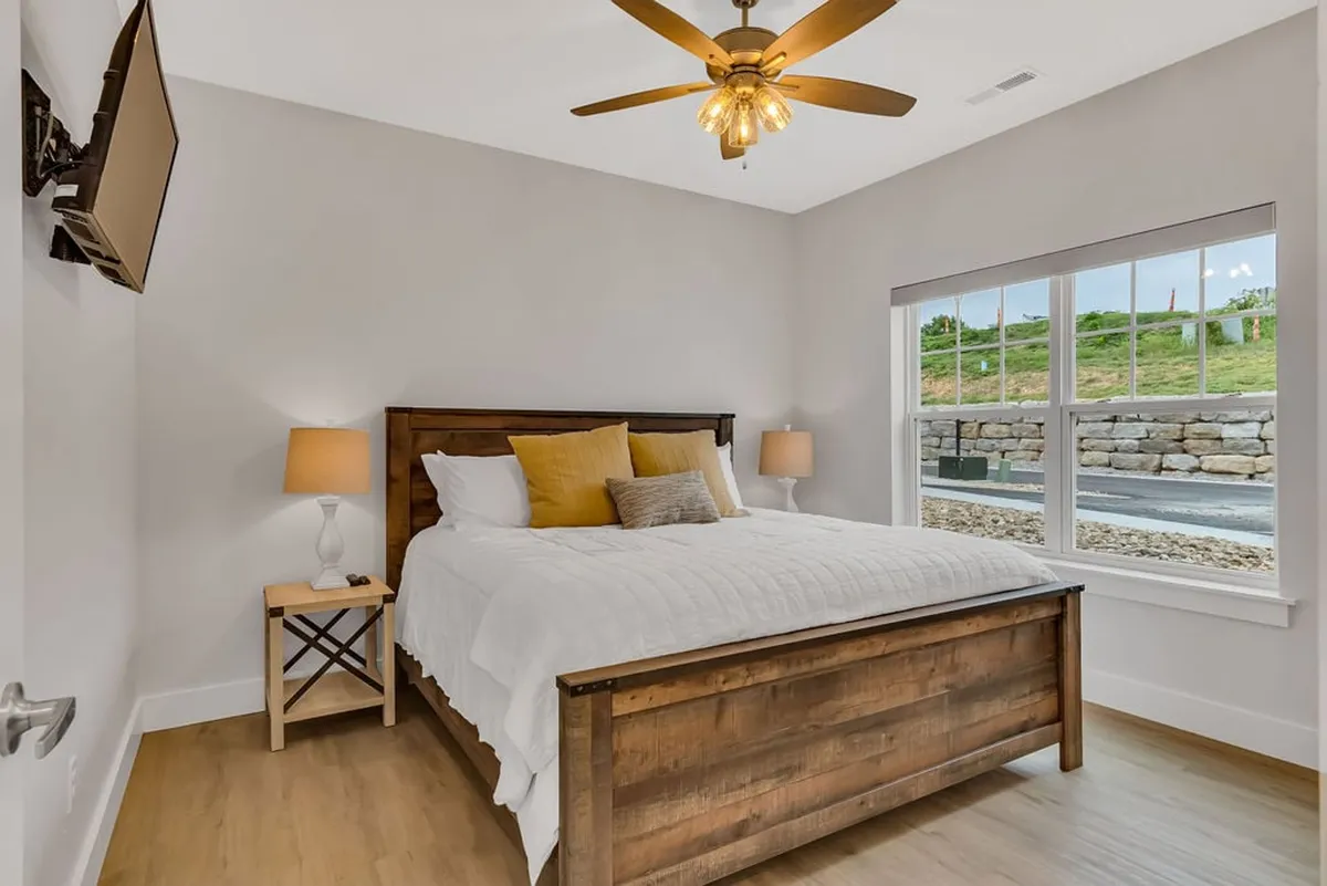 A cozy bedroom featuring a comfortable bed, a nightstand, a ceiling fan, and a window streaming in gentle sunlight. The simple, uncluttered decor promotes a calming environment ideal for winding down after a day of fun.