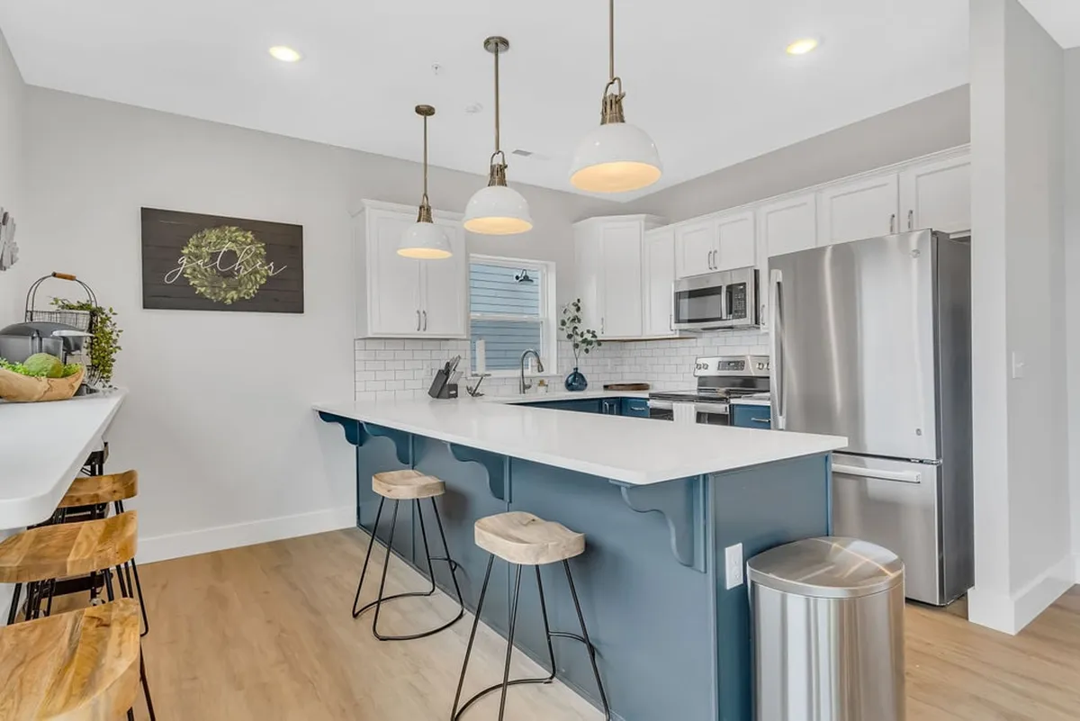 A modern, fully equipped kitchen with an expansive island, stylish pendant lighting, bar stools, and sleek appliances. The layout encourages both cooking and casual dining, while decorative elements add warmth and character to the space.