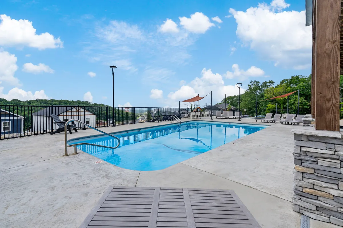 An inviting outdoor swimming pool surrounded by lounge chairs and set against a backdrop of lush landscape and a cloudy sky. The pool area is designed for relaxation and leisure, with ample space for sunbathing or socializing poolside.