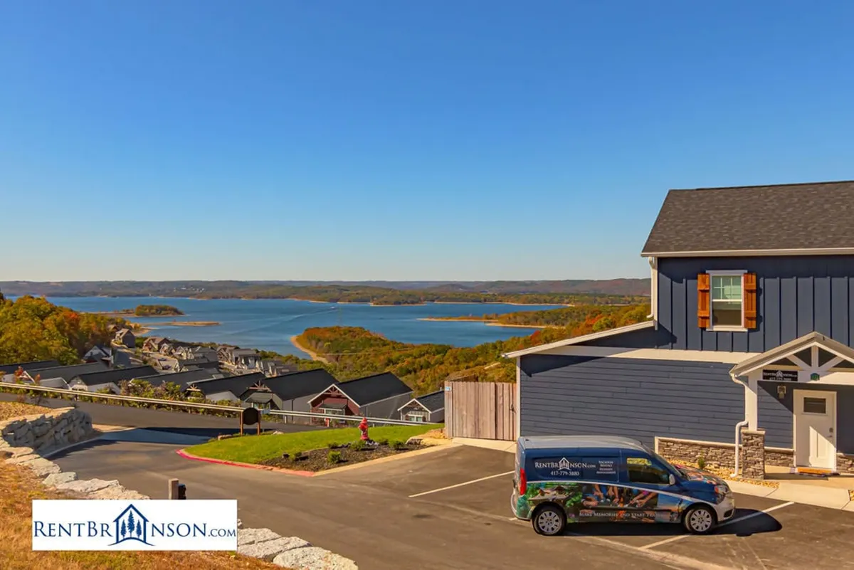 A wide-angle exterior view capturing the tranquil lake, colorful houses, and a clear blue sky. The scene includes a parking area, suggesting easy access for families embarking on outdoor adventures or returning from local attractions. The bright, inviting atmosphere hints at the vibrant lake life and scenic vistas available right outside the lodge.