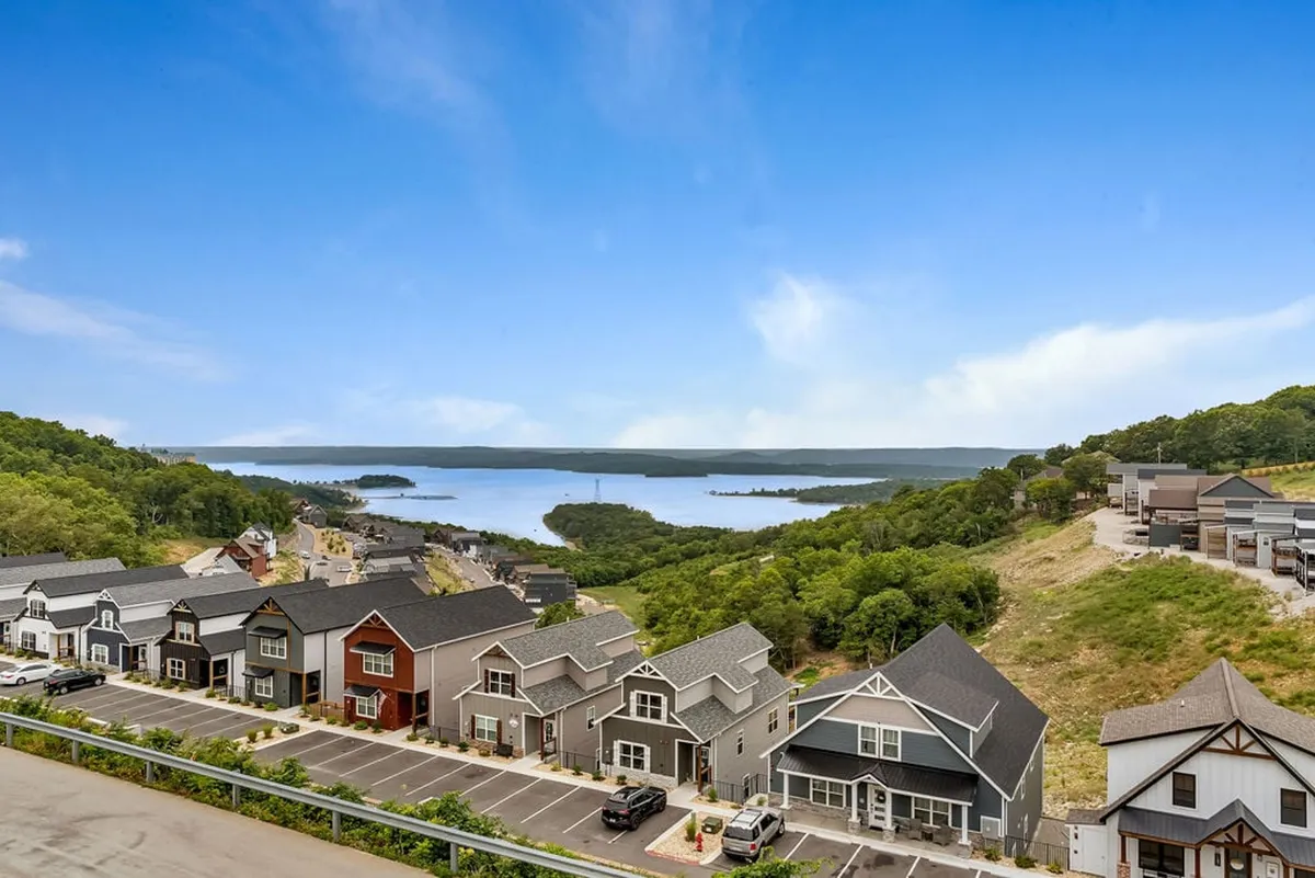 This view image captures rows of colorful houses set against an expansive lake and lush green hills. The peaceful scene suggests opportunities for boating, hiking, and gatherings outdoors, immersing guests in the scenic beauty of the Branson area.