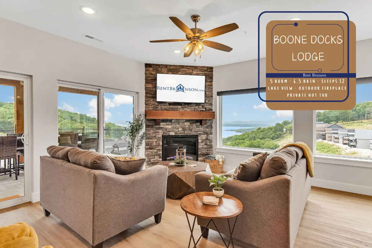 A spacious living area featuring a prominent stone fireplace, comfortable seating, and large windows that open up to a stunning view of Table Rock Lake. The warm light and cozy arrangement invite gatherings, with ample space for both relaxation and socializing.